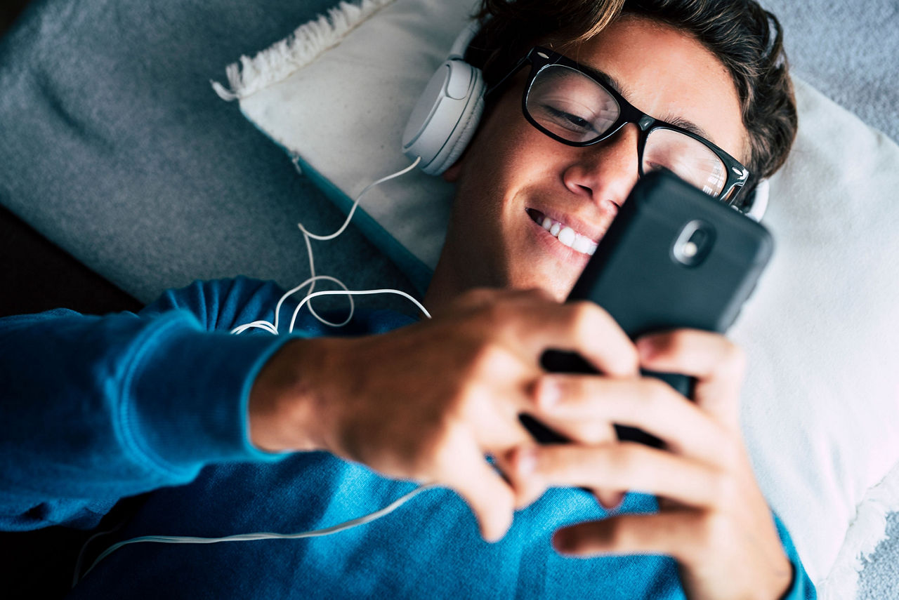 Jugendlicher hört beim Liegen mit seinem Handy Musik