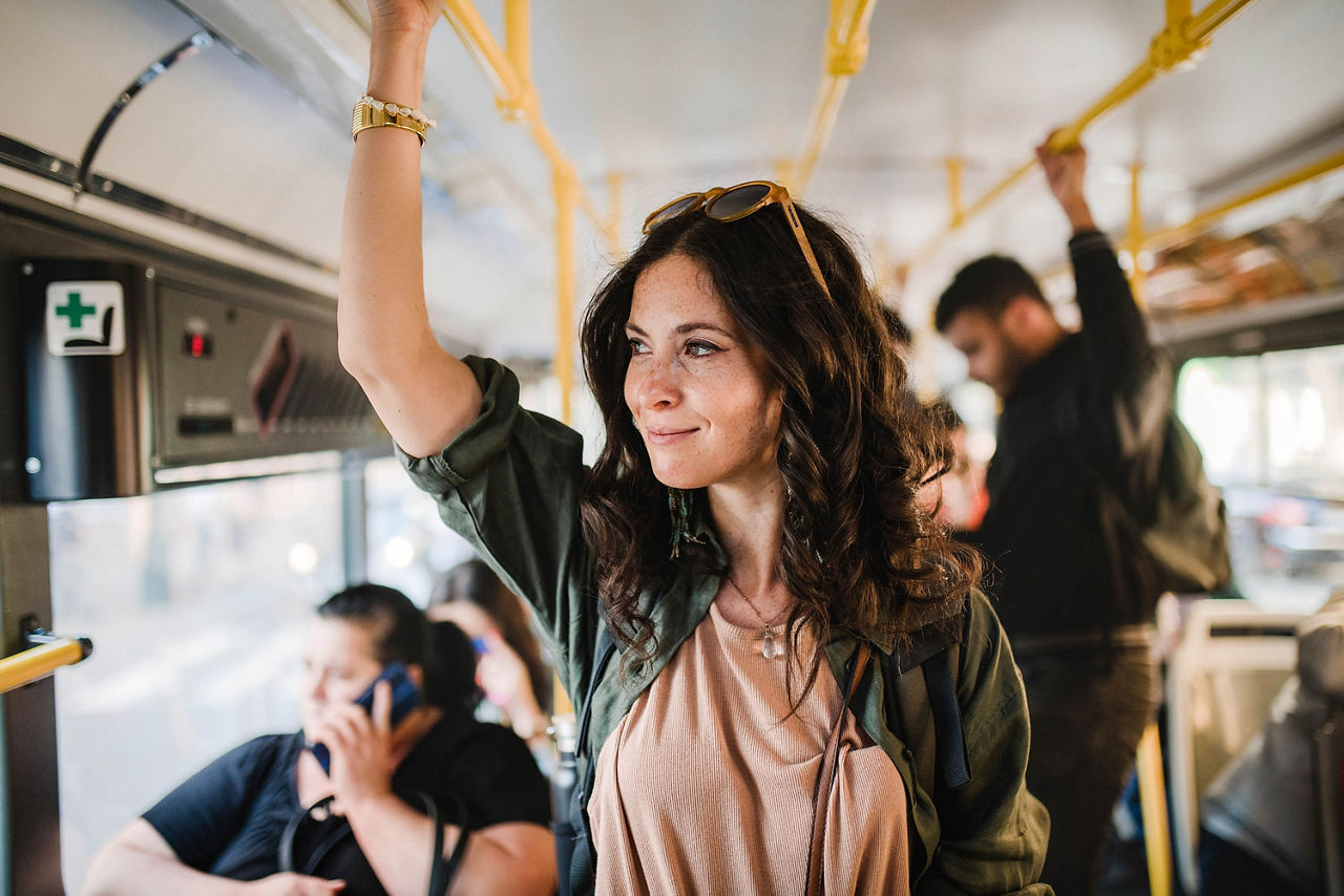 Eine mittelgroße erwachsene Frau steht im Bus und fährt mit öffentlichen Verkehrsmitteln.