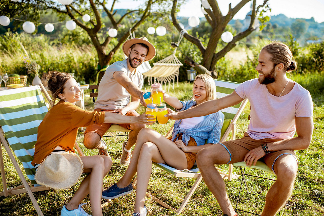 Junge und fröhliche Freunde, die sich auf den Sonnenliegen entspannen und bei einem festlichen Treffen im schön dekorierten Garten mit Gläsern anstoßen