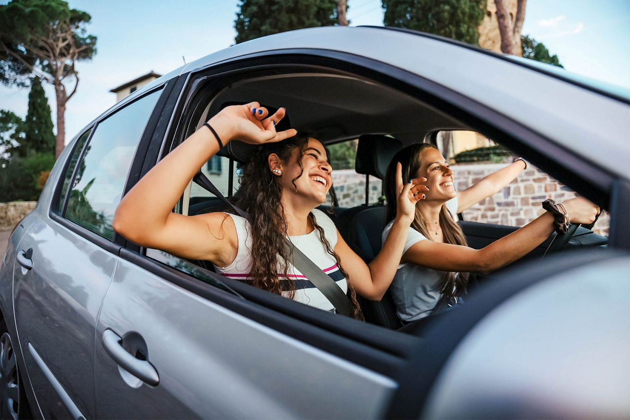 Zwei junge Frauen singen ein Lied im Radio und tanzen im Auto auf einem Tagesausflug im Sommer 
