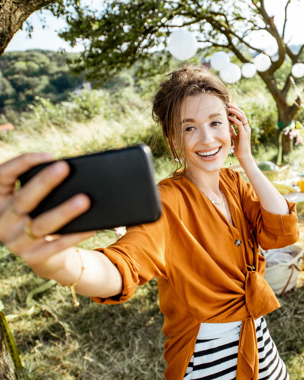 Junge Frau macht ein Selfie-Foto und hat Spaß, während sie auf das festliche Abendessen an einem schön dekorierten Ort im Hinterhof wartet
