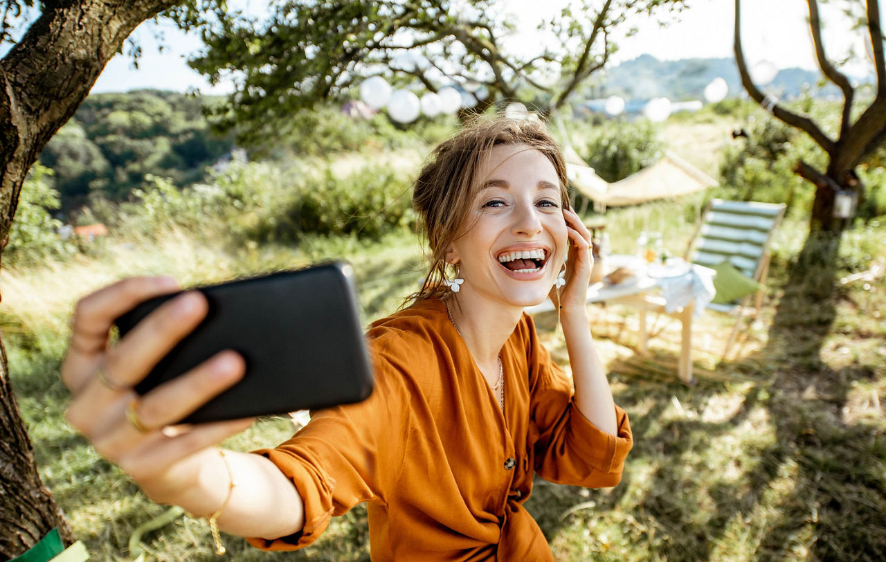 Junge Frau macht ein Selfie-Foto und hat Spaß, während sie auf das festliche Abendessen an einem schön dekorierten Ort im Hinterhof wartet