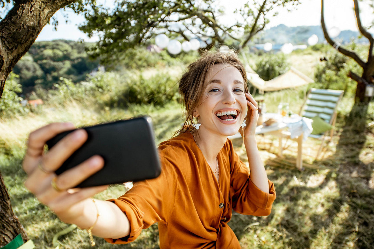 Junge Frau macht ein Selfie-Foto und hat Spaß, während sie auf das festliche Abendessen an einem schön dekorierten Ort im Hinterhof wartet