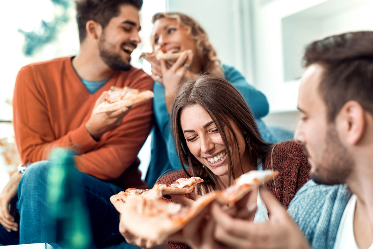 Eine Gruppe von Freunden sitzen Zuhause zusammen und essen Pizza. 