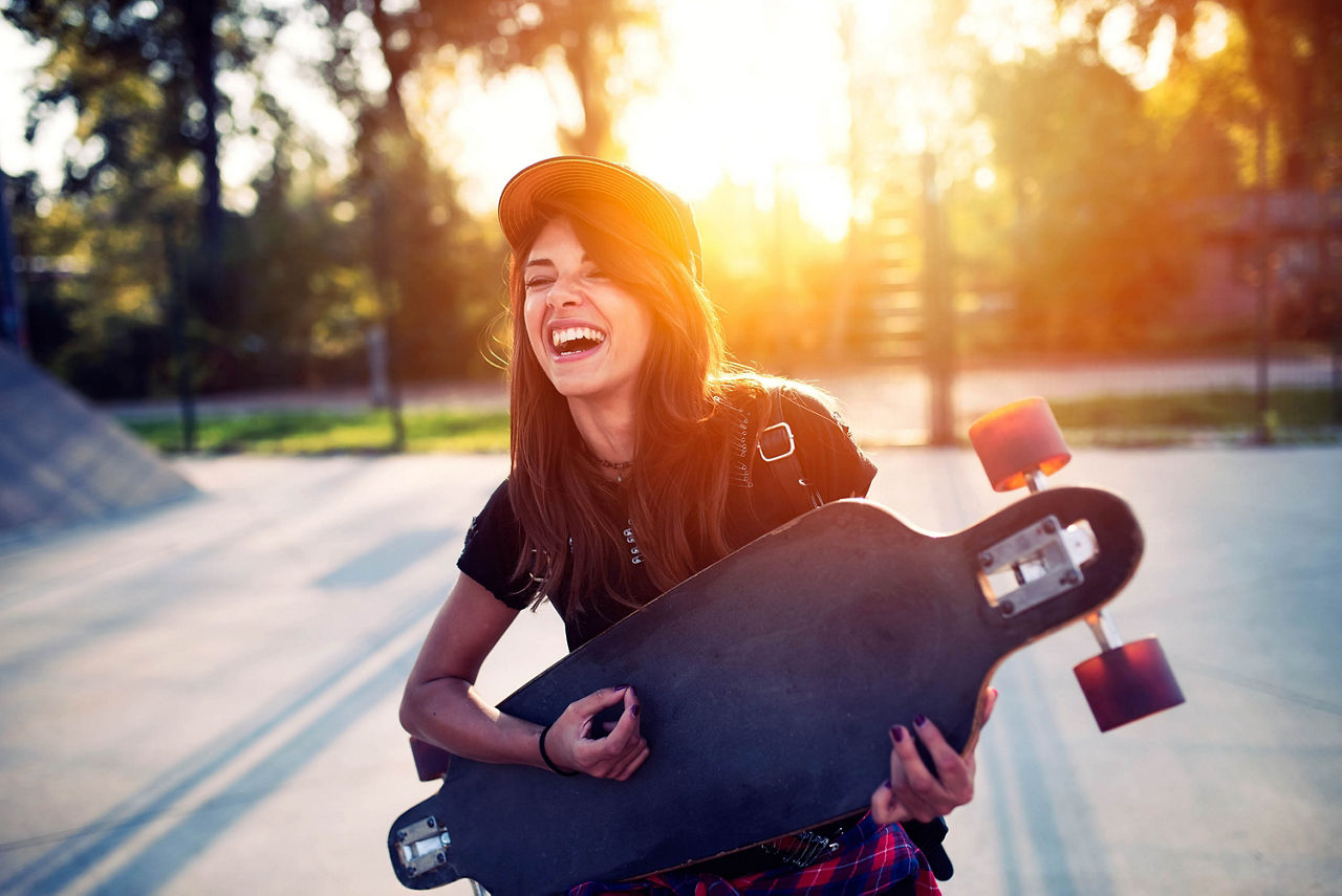 Nettes Mädchen hält Skateboard im Skatepark in der Hand und spielt darauf Gitarre