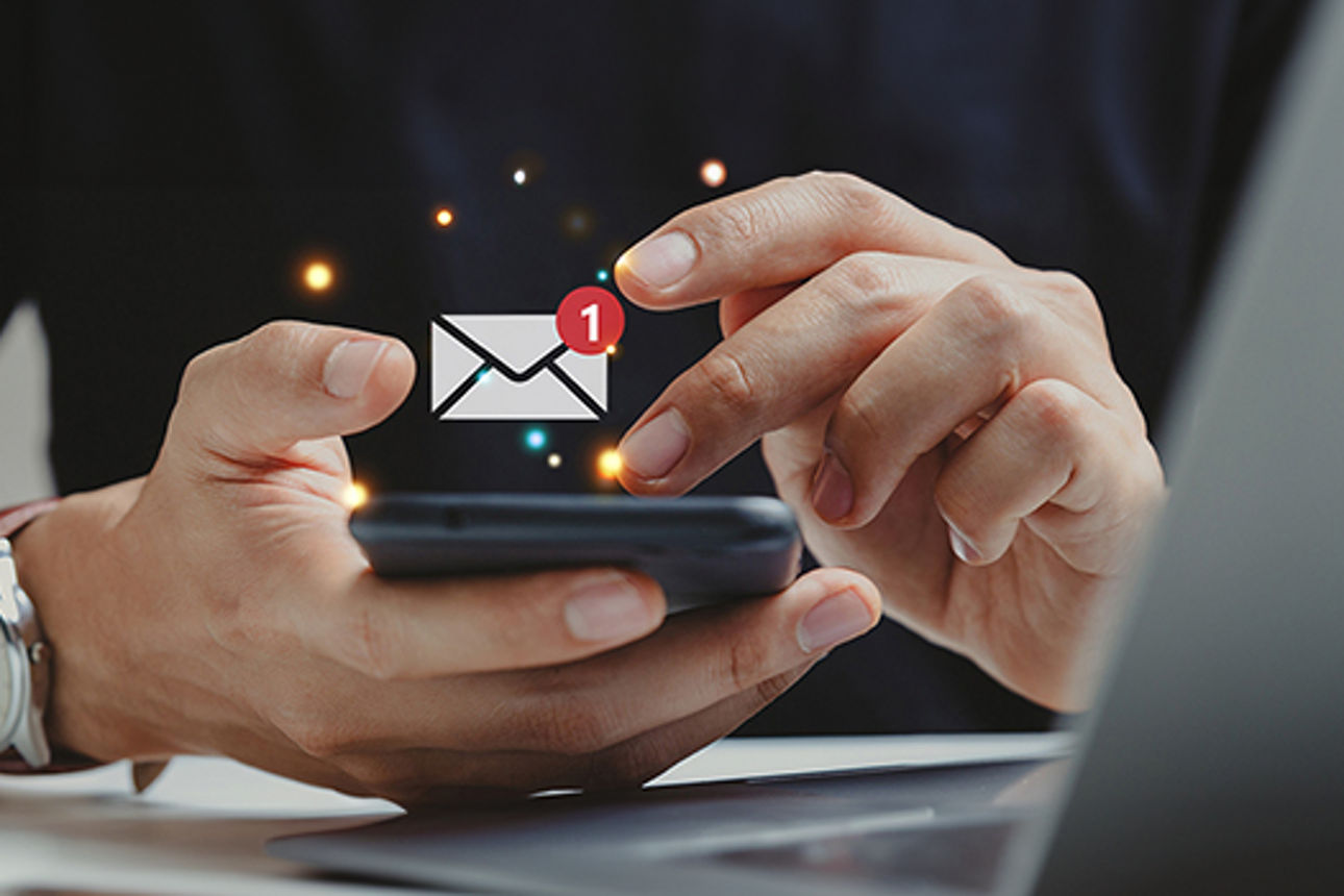 Mensch hält ein Handy mit einem E-Mail Icon drüber
