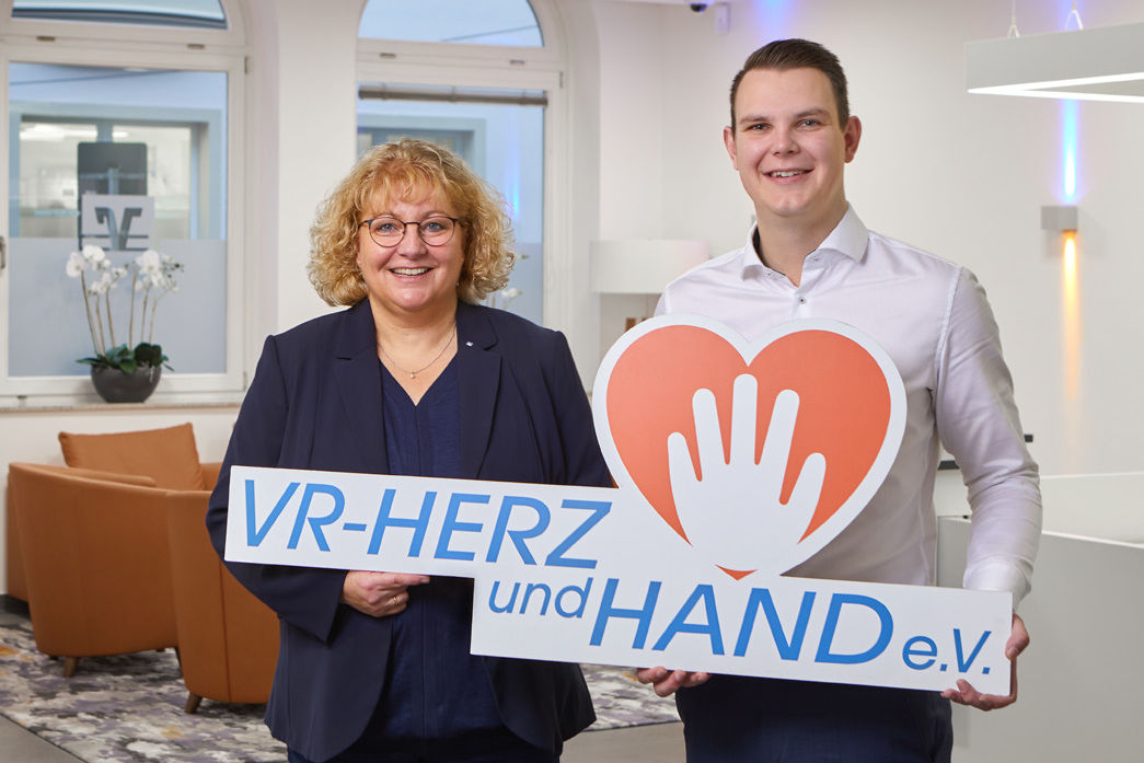 Zwei Mitarbeiter halten das Logo von VR-Herz und Hand e.V. in der Hand