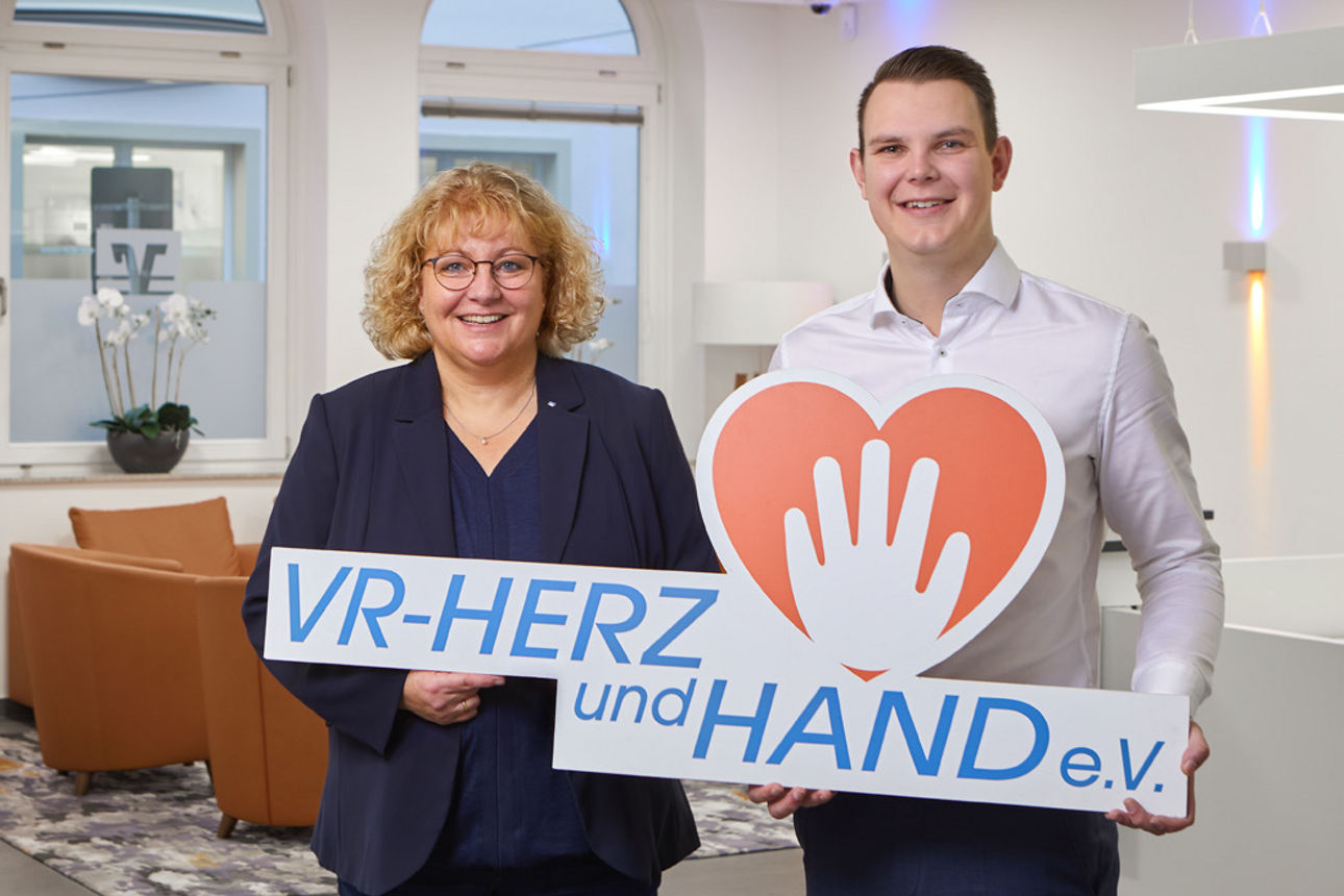Zwei Mitarbeiter halten das Logo von VR-Herz und Hand e.V. in der Hand