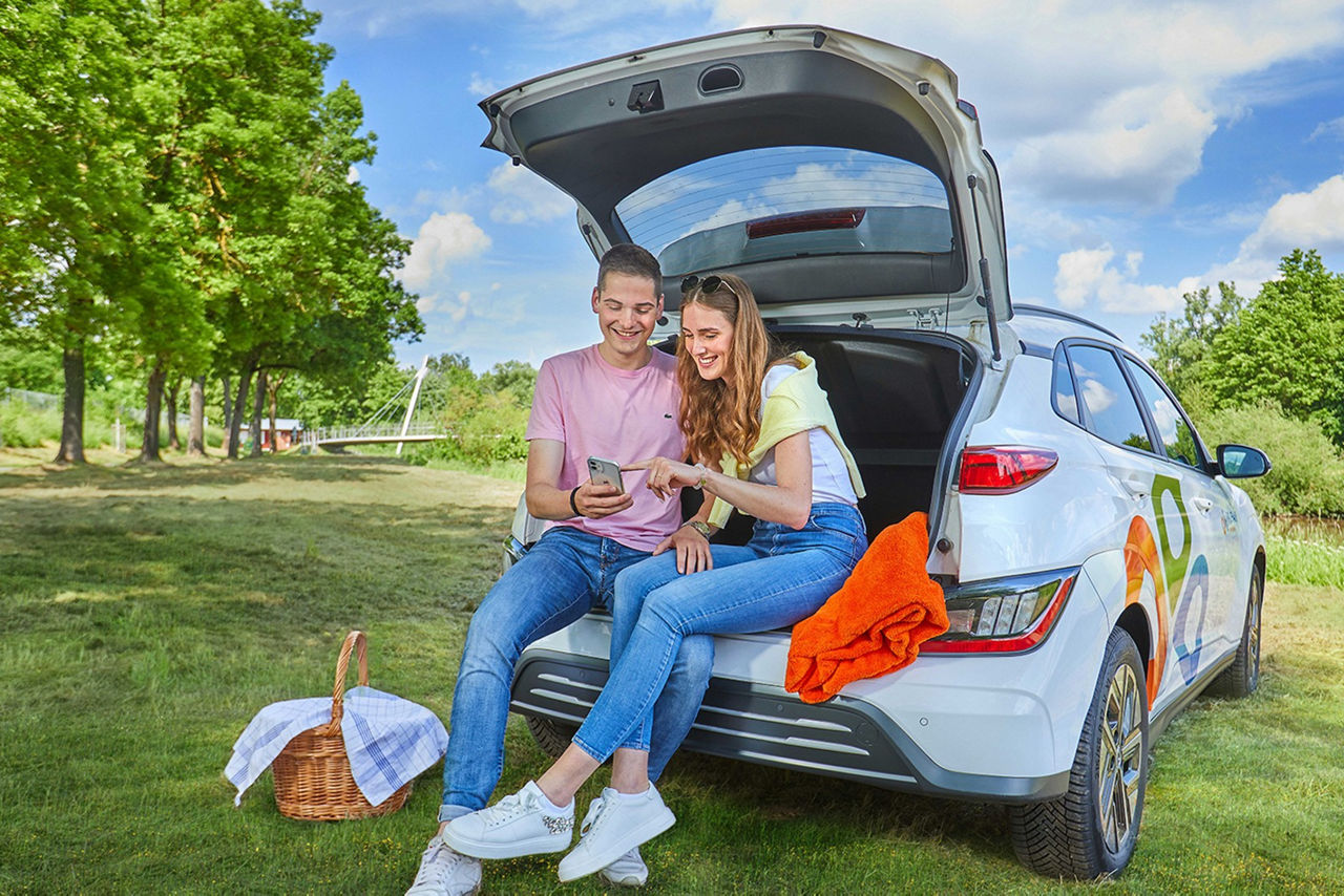 Zwei Frauen sitzen in dem Kofferraum eines VR-Share Autos und Picknicken 
