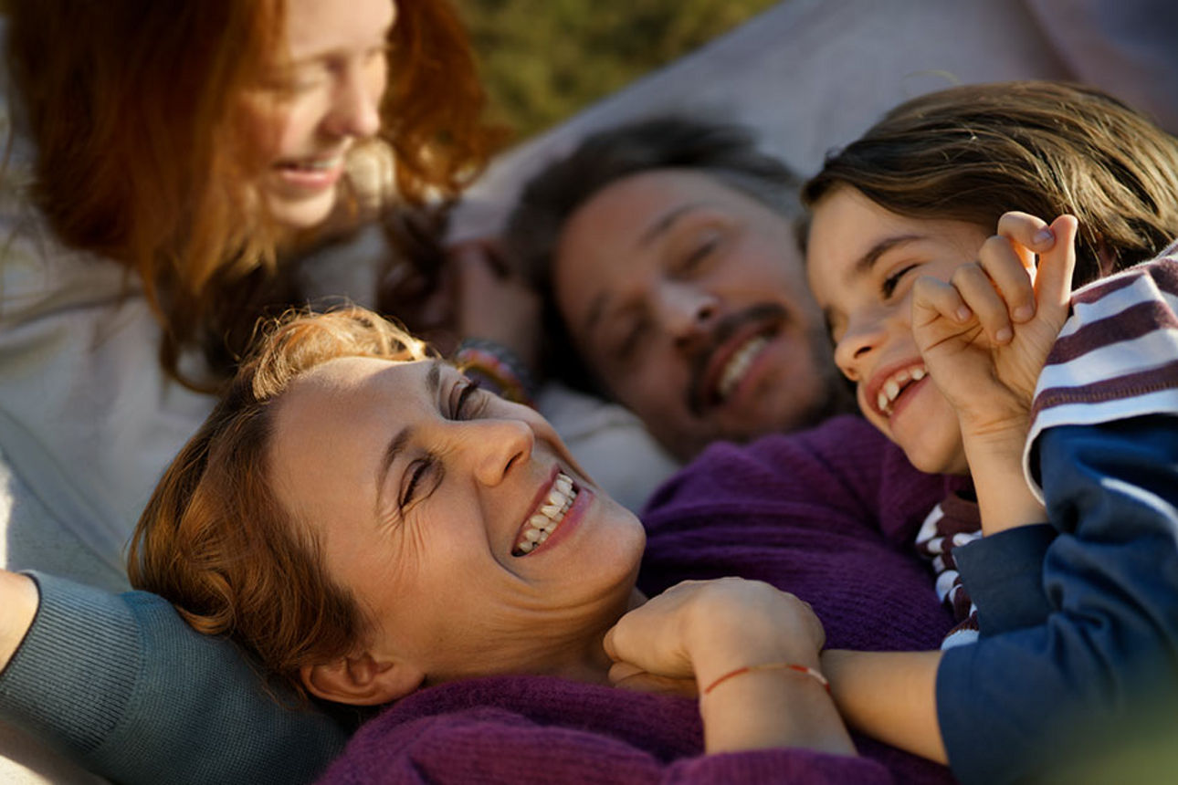 Eine Frau kuschelt mit ihrer Familie. Alle lachen.