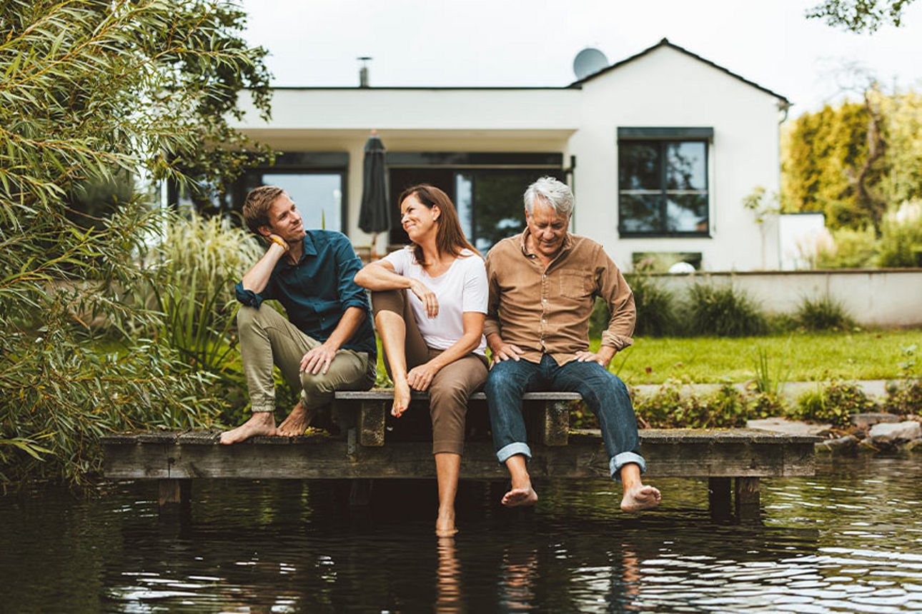 Eine Familie sitzt am Ufer im Garten ihres Hauses.