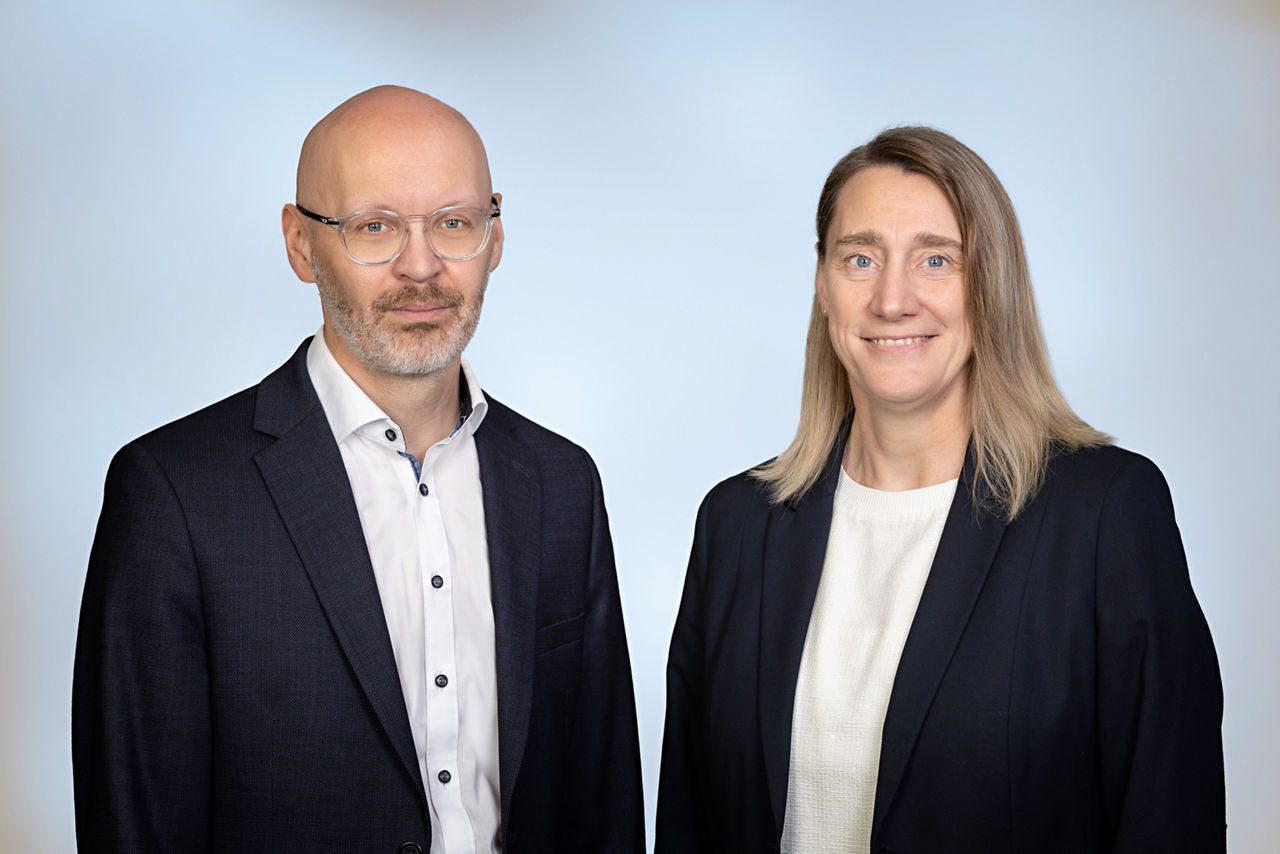 Ein Mann und eine Frau in Anzügen vor weißem Hintergrund.