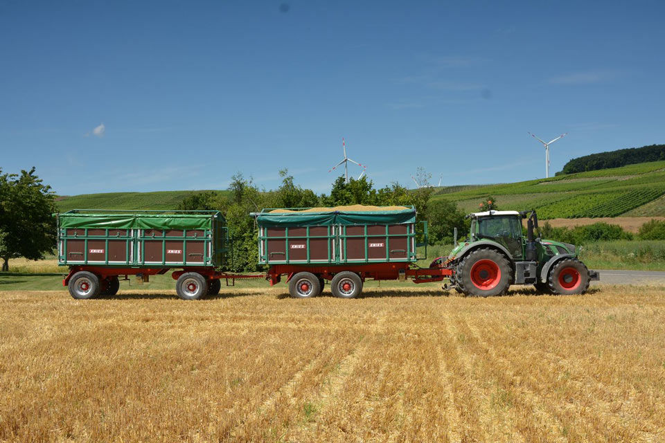 Ein Traktor mit zwei Anhängern fährt über ein Stoppelfeld.