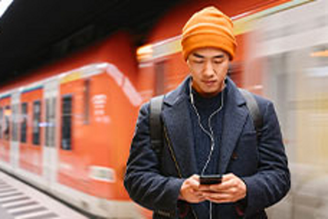 Mann in einer U-Bahn-Station, der auf sein Smartphone schaut