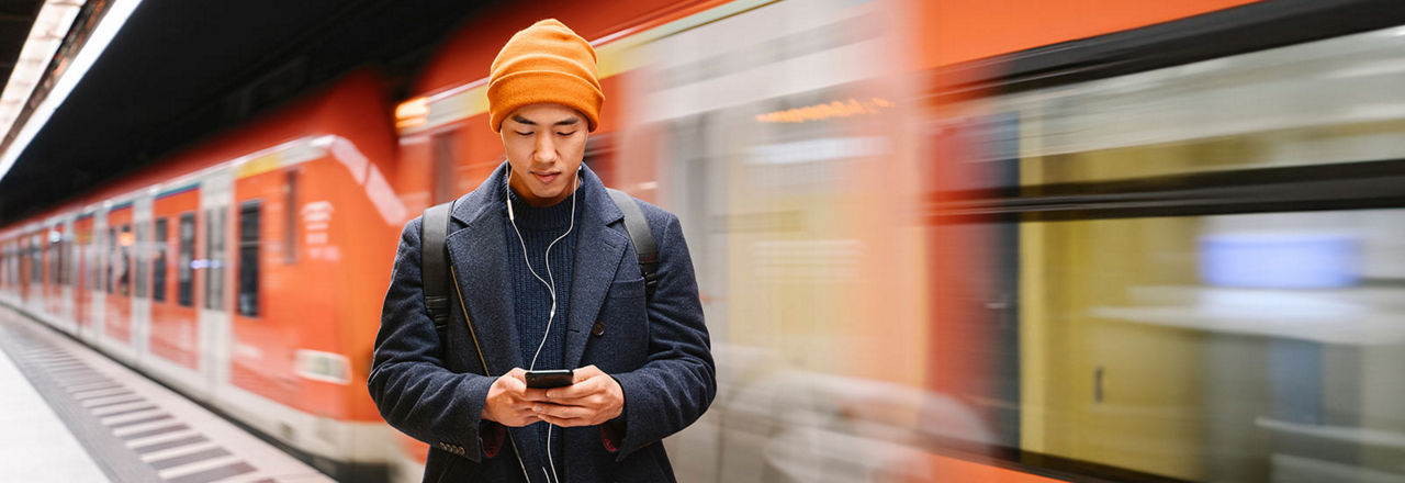Mann schaut auf Smartphone und im Hintergrund fährt eine U-Bahn vorbei
