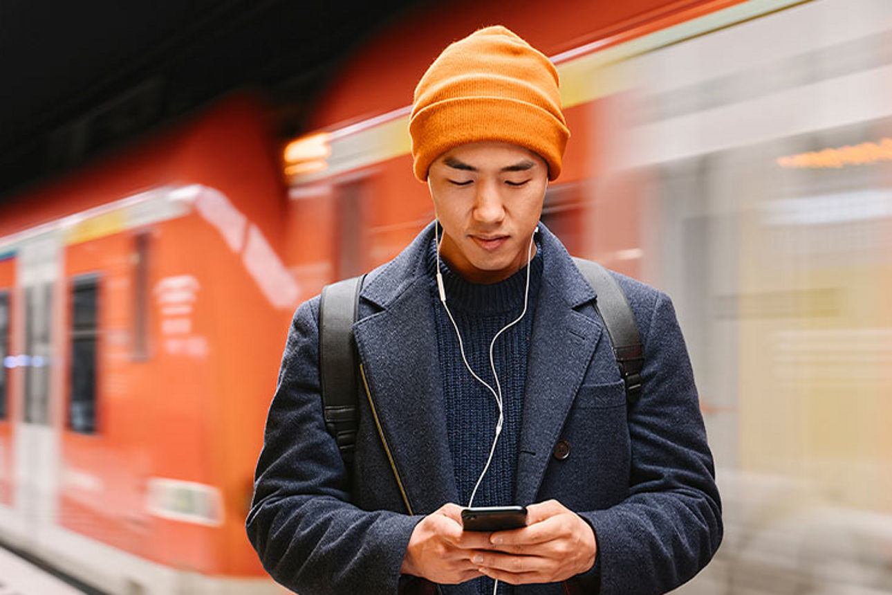 Mann schaut auf Smartphone und im Hintergrund fährt eine U-Bahn vorbei
