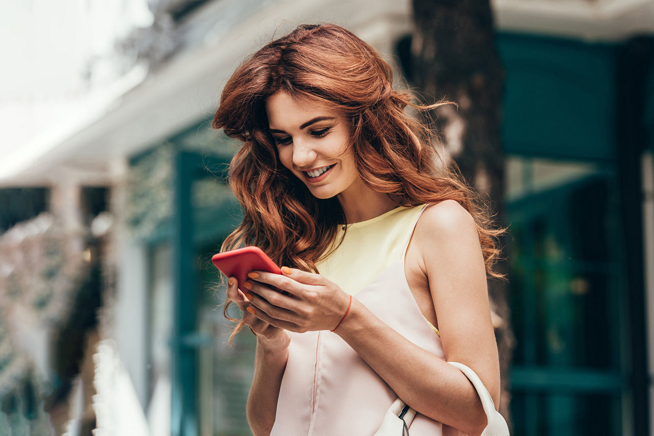 Junge Frau mit roten Haaren blickt lächelnd auf Ihr Smartphone