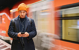 Junger Mann am Bahngleis mit Handy in der Hand