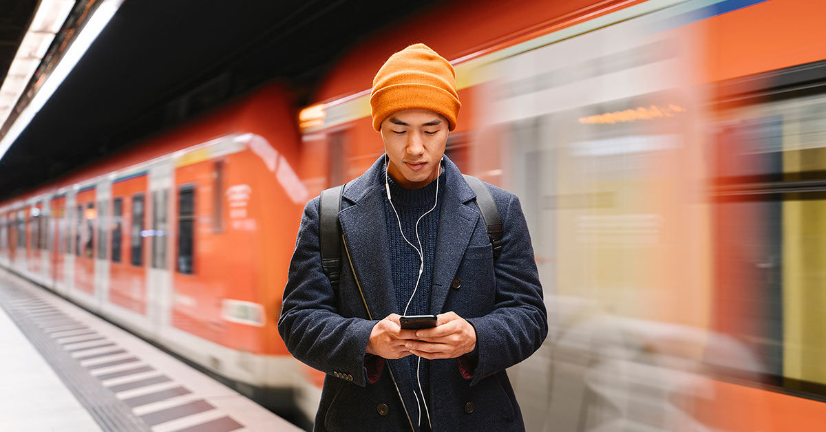 Junger Mann steht am Bahnsteig und schaut auf sein Smartphone 