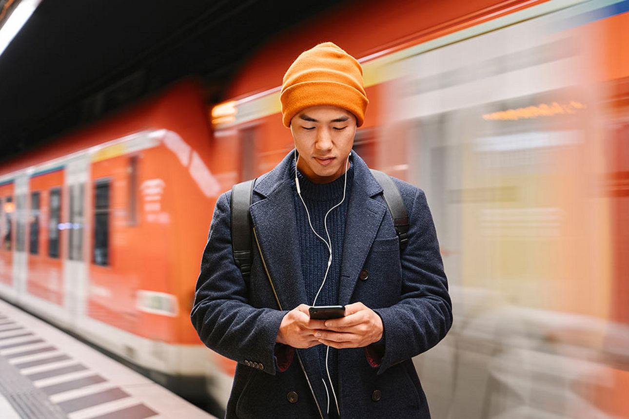 Junger Mann steht am Bahnsteig und schaut auf sein Smartphone 