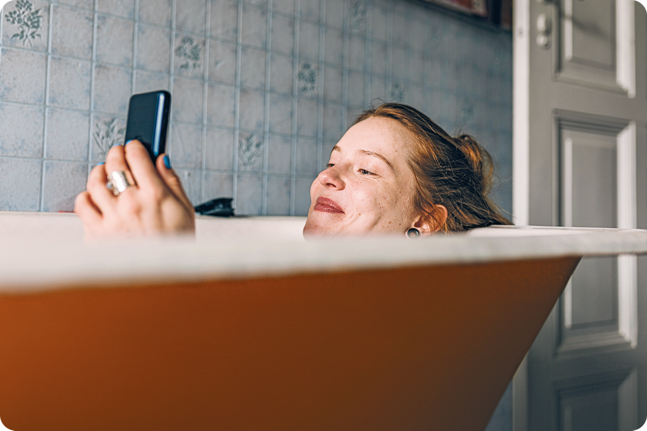 Ein Frau liegt in der Badewanne und schaut lächelnd auf ihr Smartphone