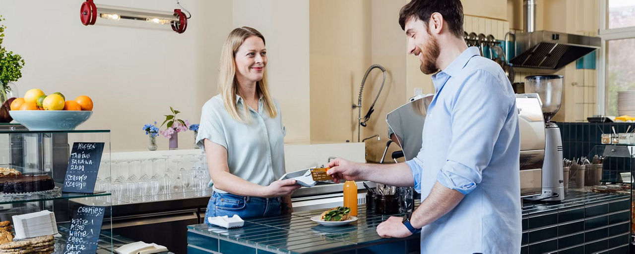 Ein Mann zahlt in einem Geschäft mit seiner Bankkarte die Verkäuferin lächelt