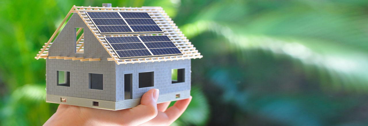 Eine Hand hält ein kleines Modelhaus mit Solarpanels