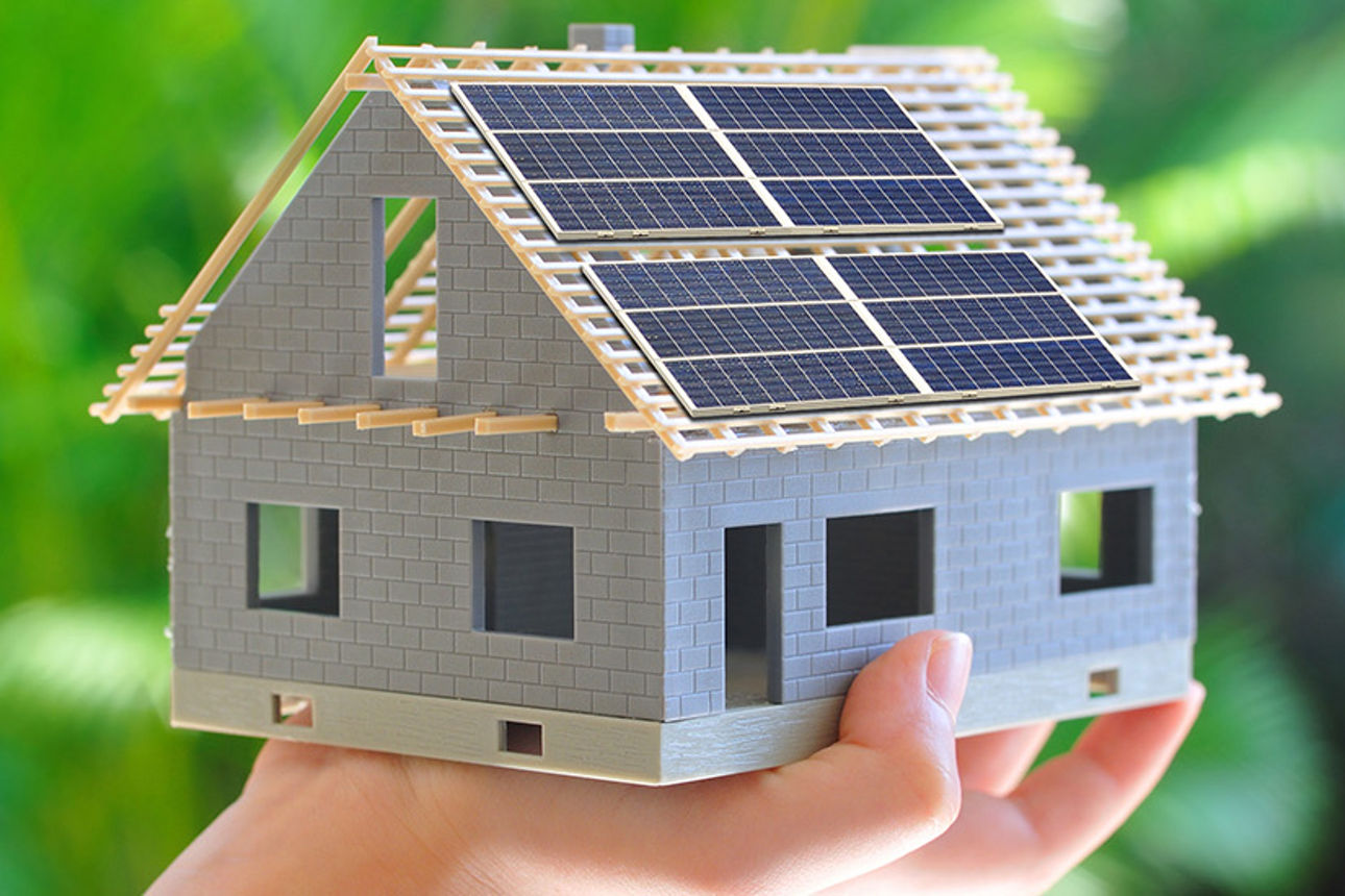 Eine Hand hält ein kleines Modelhaus mit Solarpanels