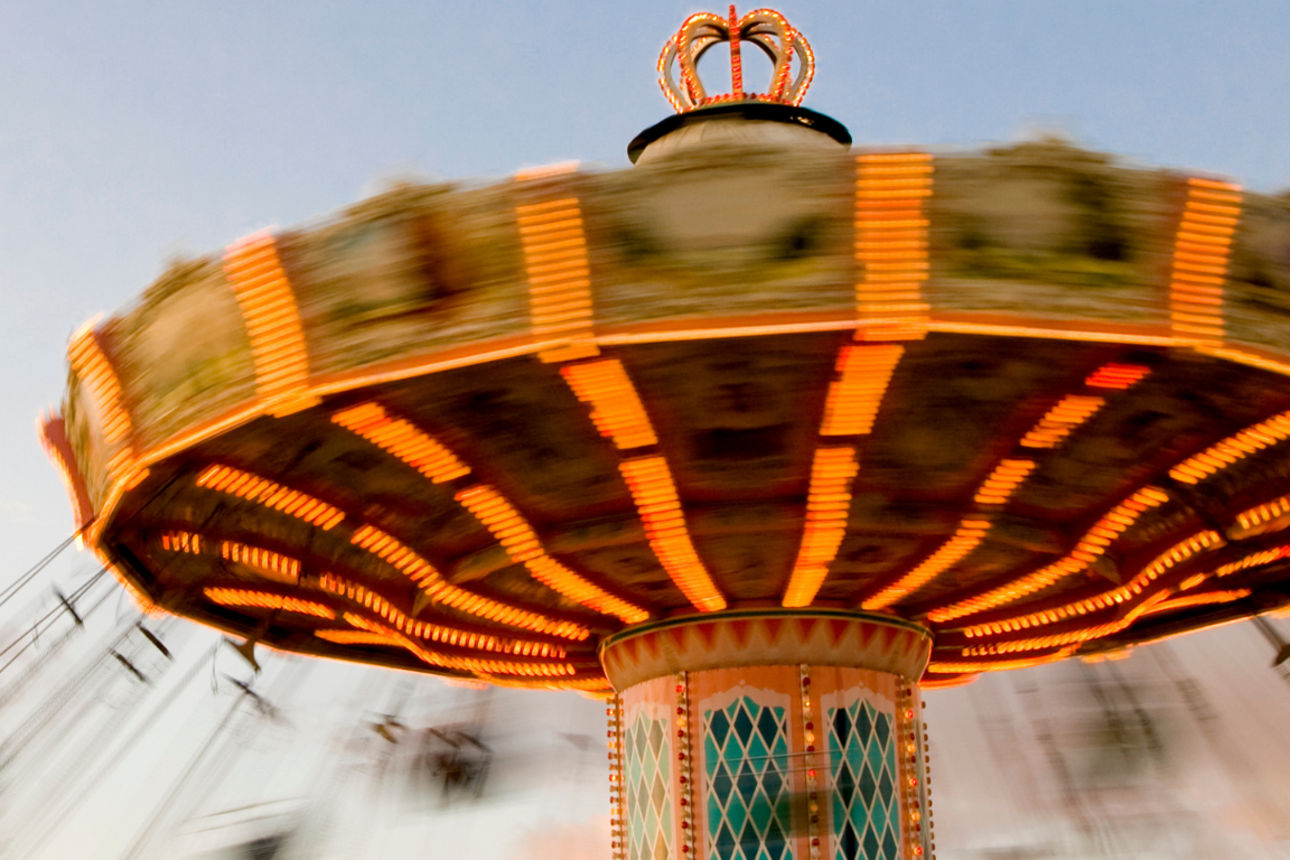 Beleuchtetes Kettenkarussell in Bewegung vor Abendhimmel, daneben Logos von Europa-Park und Erlebnispark Tripsdrill.