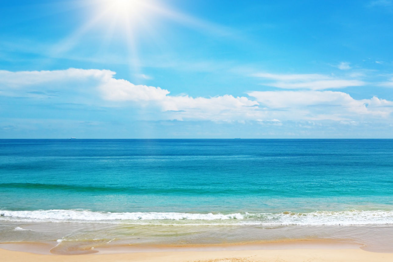 Blick über einen Sandstrand auf türkisblaues Meer und Sonne