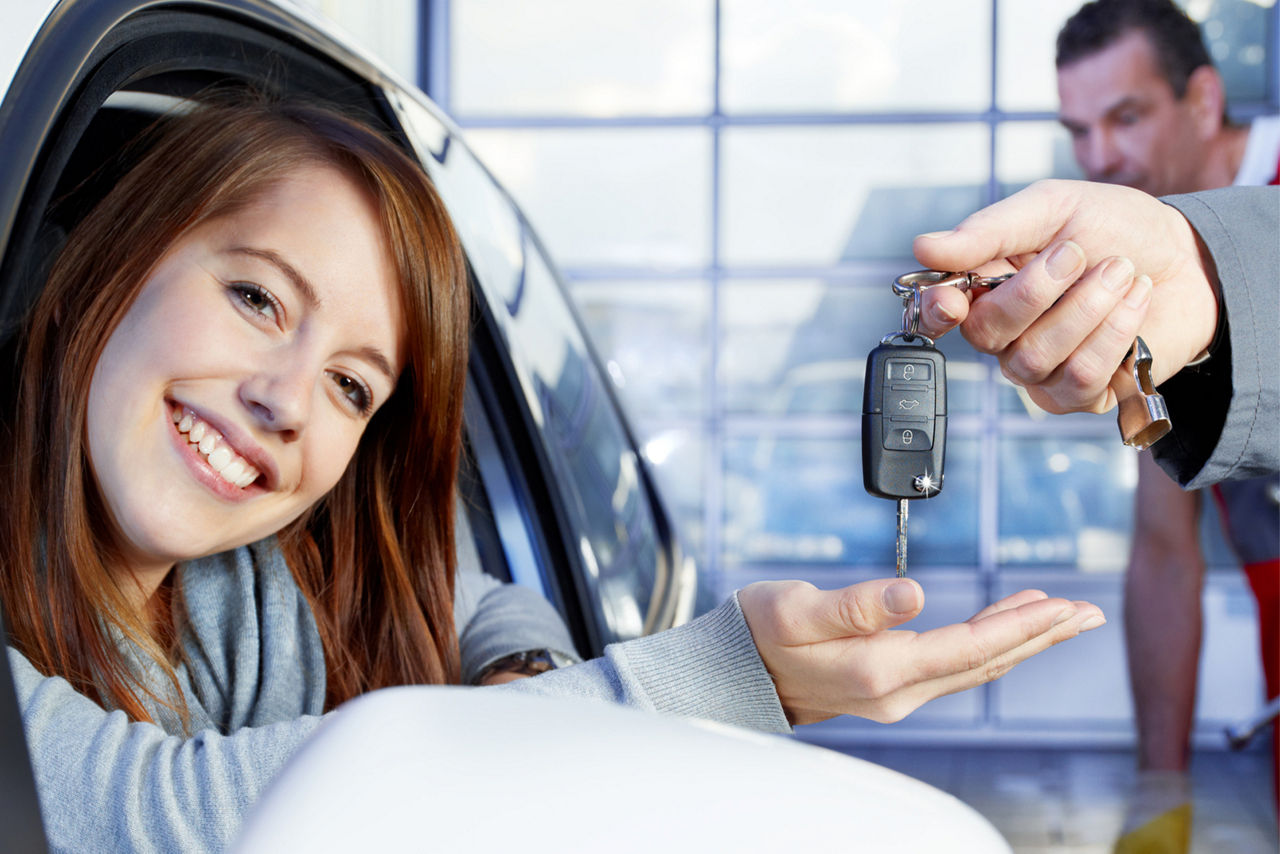 Eine junge Frau lächelt breit, als sie die Schlüssel für ihr neues Auto entgegennimmt