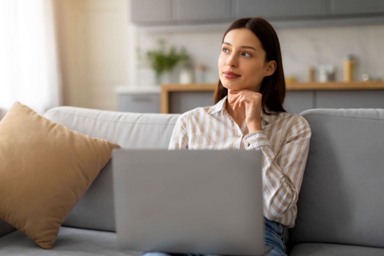Frau mit Laptop sitzt nachdenklich auf der Couch