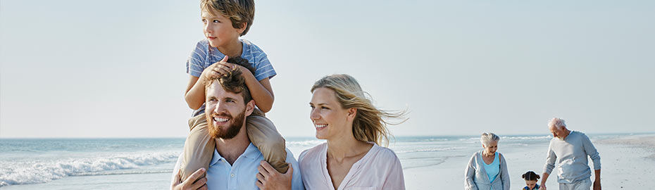 Eine Familie genießt einen sonnigen Tag am Strand und spielt zusammen mit ihrem Kind im Sand und in der Brandung.