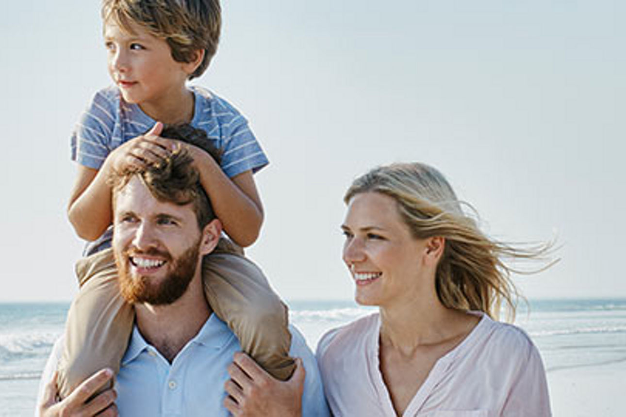 Eine Familie genießt einen sonnigen Tag am Strand und spielt zusammen mit ihrem Kind im Sand und in der Brandung.