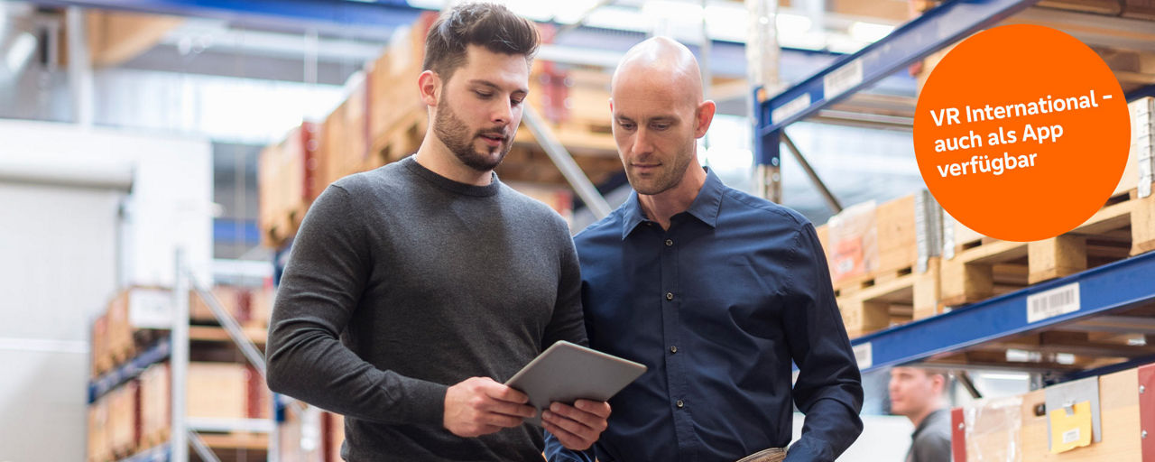 Zwei Männer bei der Arbeit in einer Lagerhalle schauen gemeinsam auf ein Tablet