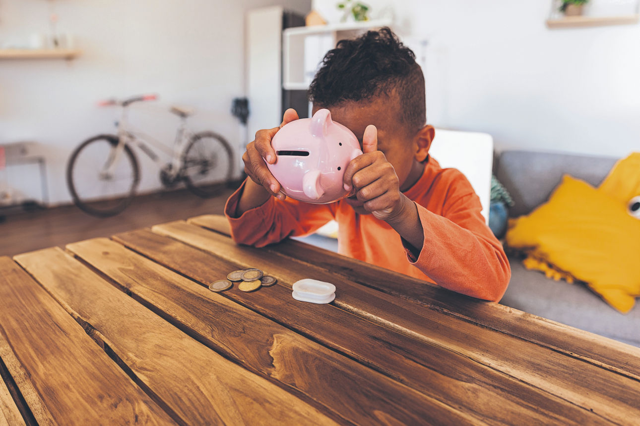 Kind leert sein Sparschwein und zählt Münzen am Holztisch