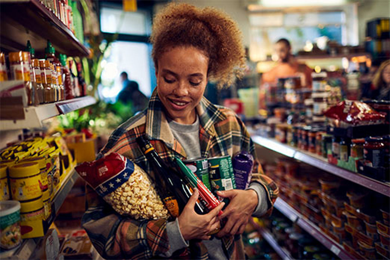 Frau im Supermarkt hält Lebensmittel im Arm Frau im Supermarkt hält Lebensmittel im Arm