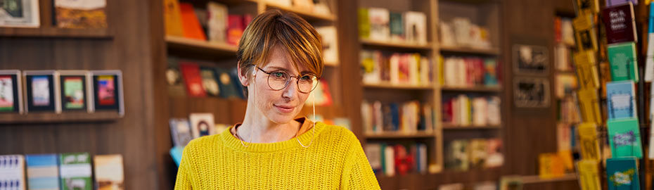 Eine Frau mit Brille und gelbem Pullover vor einer Bibliothek mit Büchern
