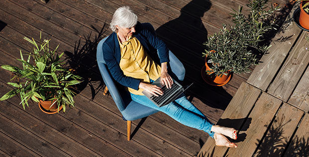 Frau sitzt entspannt mit einem Laptop auf der Terrasse