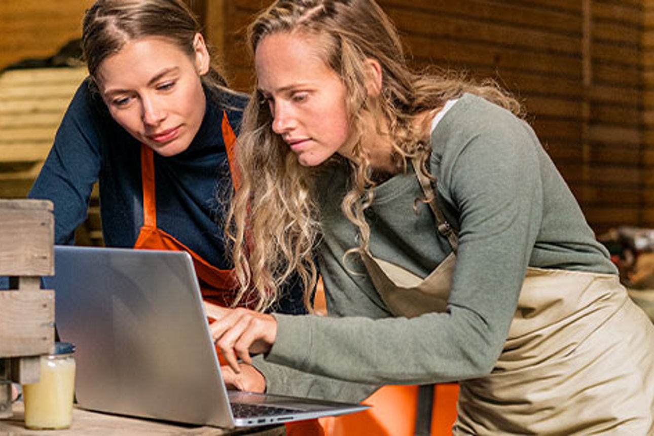 Zwei junge Frauen stehen in einer Werkstatt und schauen auf ein Notebook