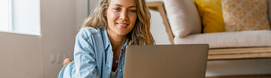 Frau liegt auf dem Boden und schaut in ihren Laptop