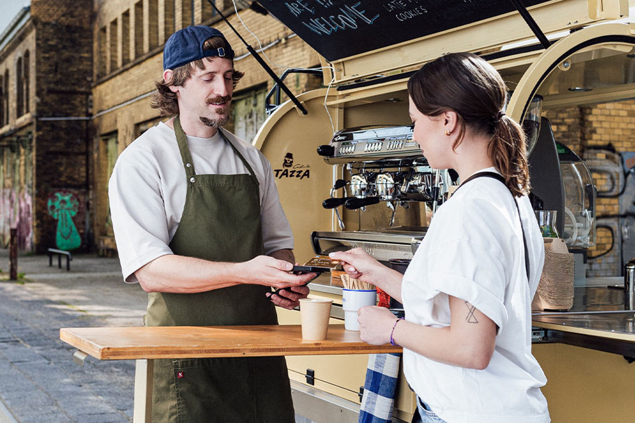 Eine Frau bezahlt einen Kaffee an einem Kaffeestand