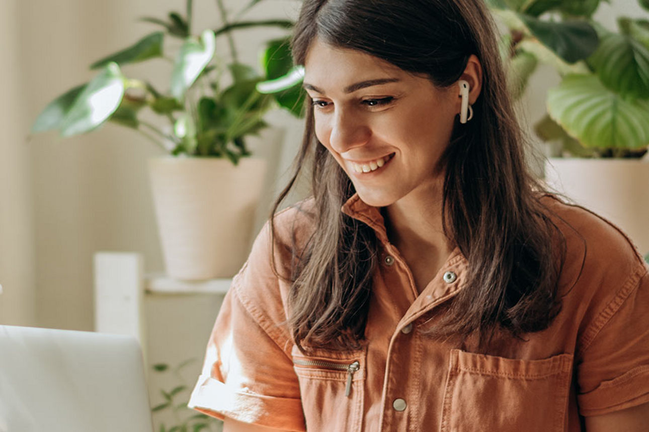 Junge Frau sitzt in einem hellen Raum mit Handy am Laptop am Tisch