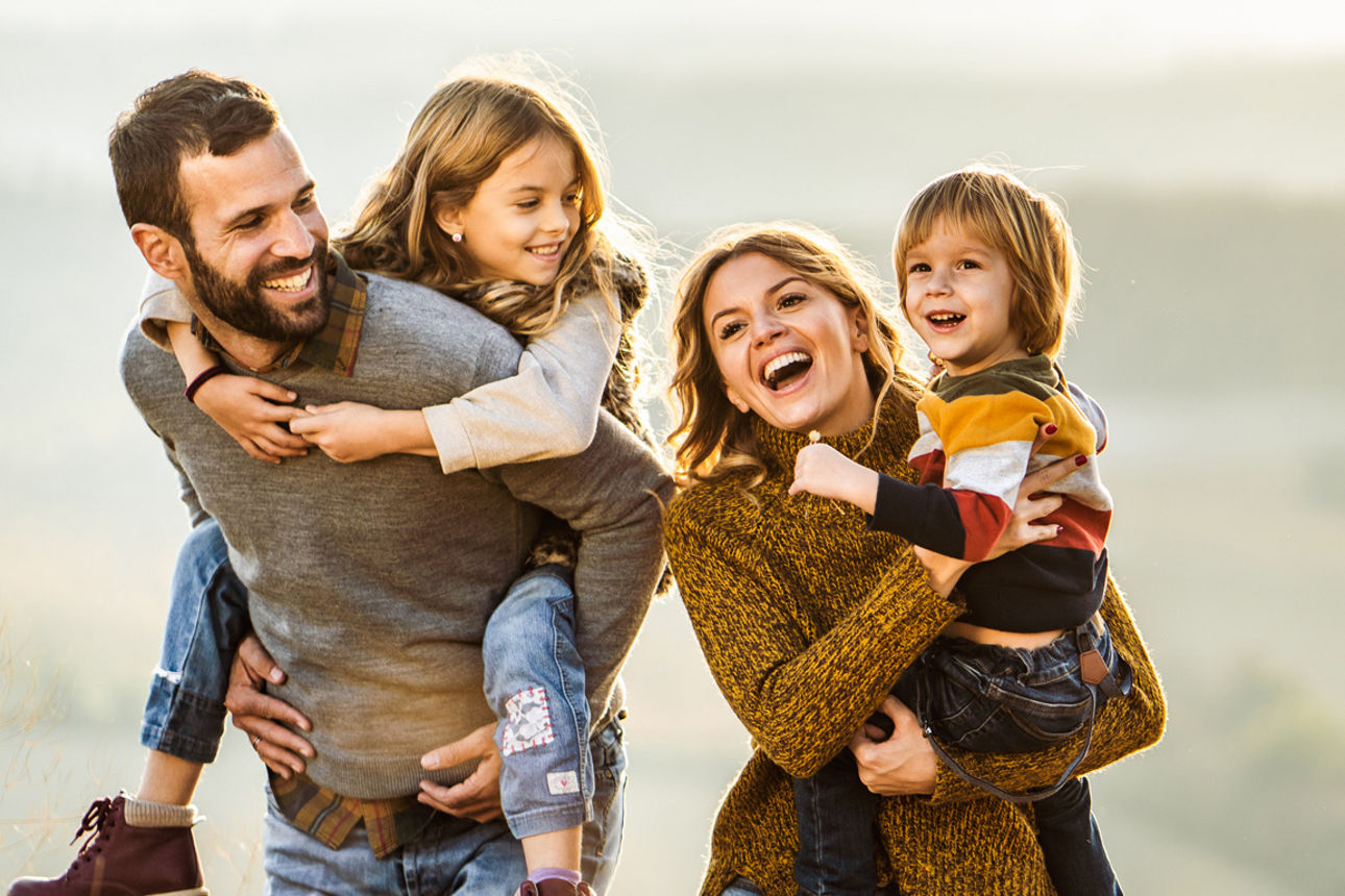 Glückliche Famile macht einen Spaziergang. Die Kinder werden von den Eltern getragen.