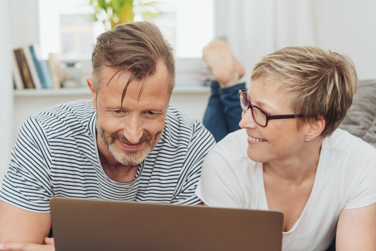 Mann und Frau liegen auf dem Sofa und schauen in Laptop