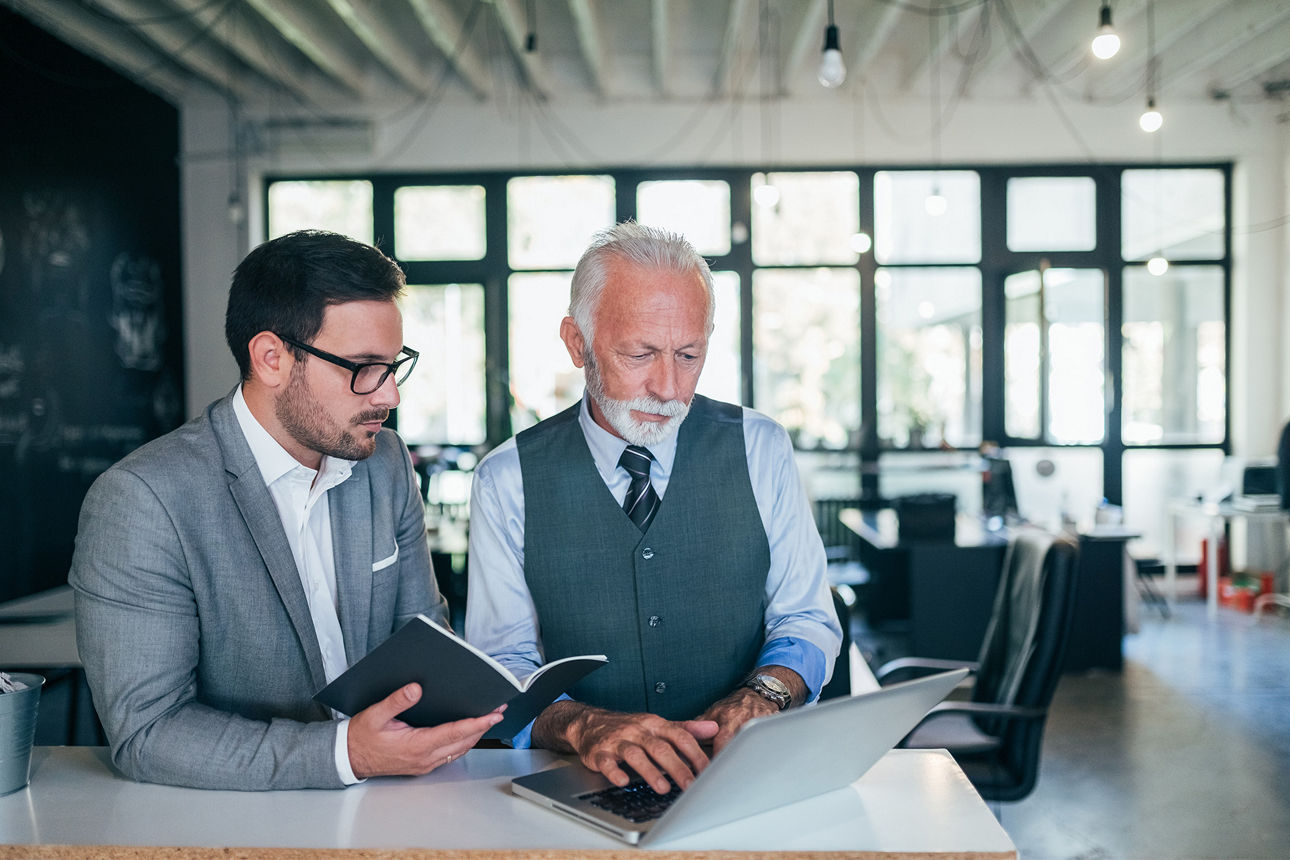 Zwei Geschäftsmänner in einem Büro schauen gemeinsam auf ein Notebook.