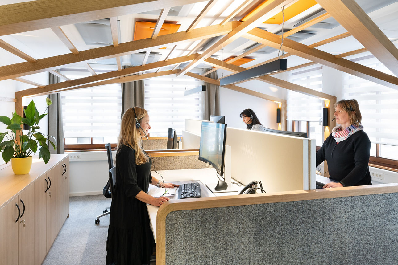Zwei blonde Damen an Schreibtischen mit Headsets auf dem Kopf in einem Büroraum