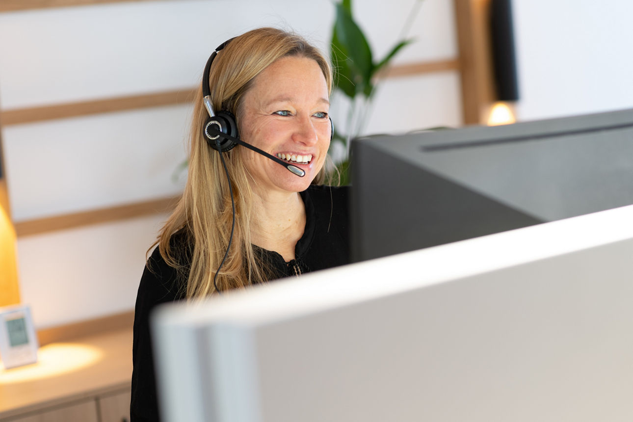 Blonde Frau mit Kopfhörern hinter Computer-Bildschirm im Büro