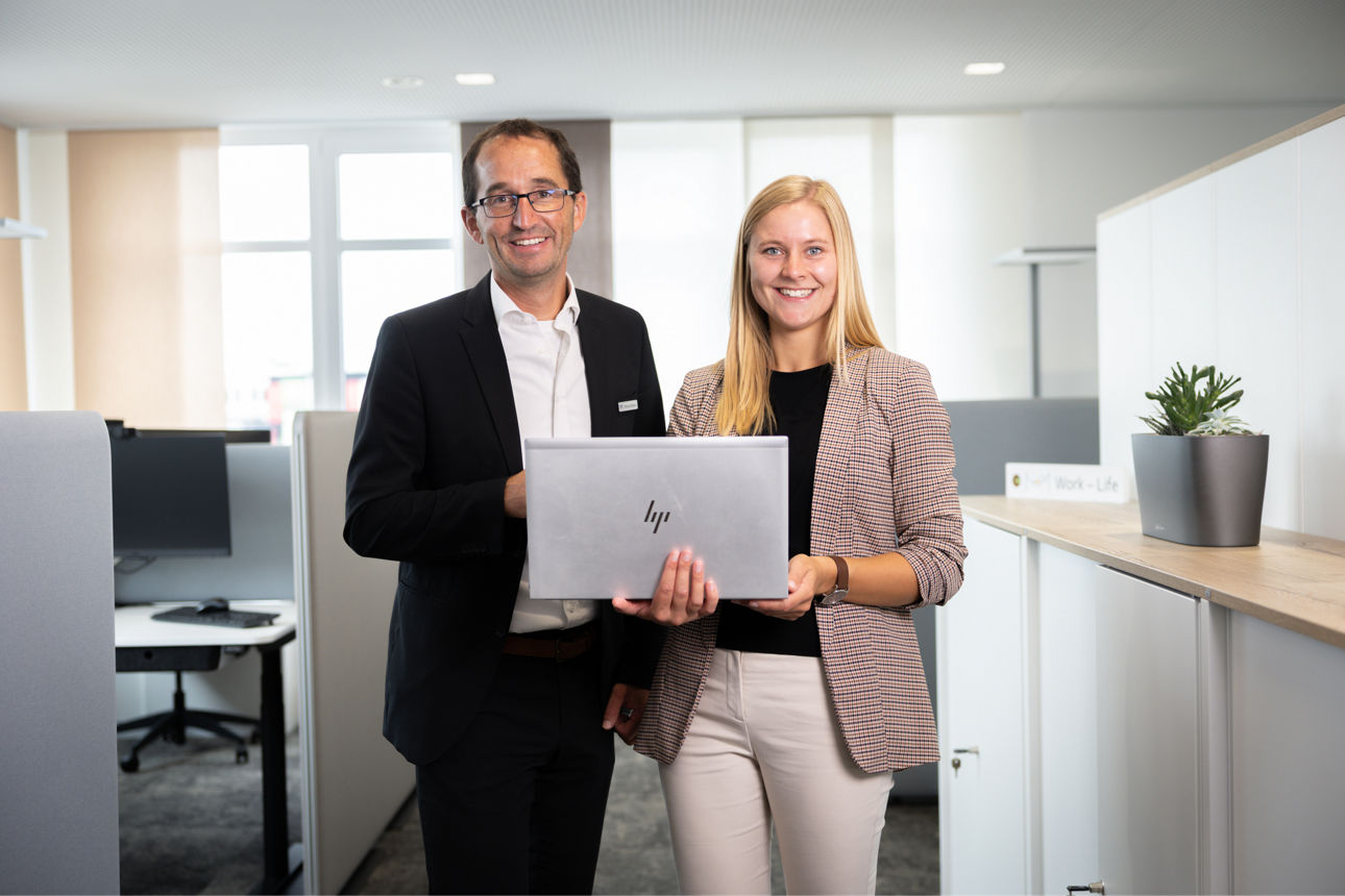 Zwei Arbeitskollegen stehen in einem  freundlichen Büro mit einem Laptop