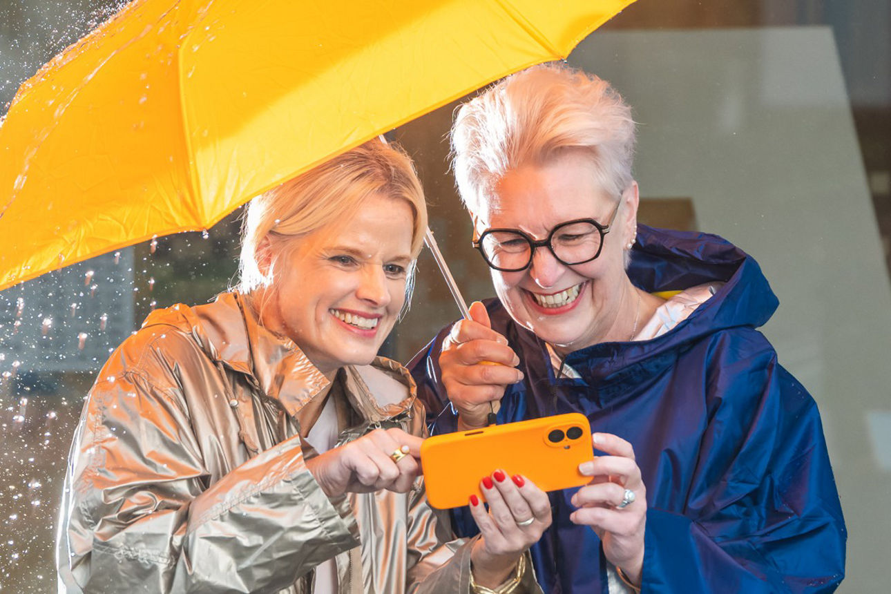 Zwei Frauen unter einem Regenschirm schauen auf ein Smartphone